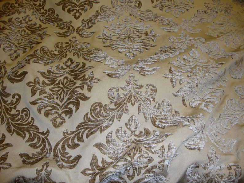 Pu&ograve; includere: Un tessuto beige con un motivo damascato marrone. Il tessuto ha una leggera lucentezza e una superficie testurizzata.