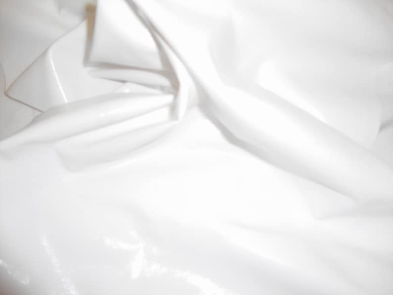 Peut inclure: Un tissu blanc uni avec une surface lisse, brillante et r&eacute;fl&eacute;chissante. Le mat&eacute;riau est drap&eacute; en plis doux et fluides, cr&eacute;ant des reflets et des ombres qui soulignent sa texture brillante semblable &agrave; du vinyle et sa couleur blanche uniforme.