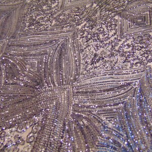 May include: A close-up of a silver sequined fabric with a geometric pattern. The sequins are arranged in a series of vertical lines and squares, creating a shimmering effect.