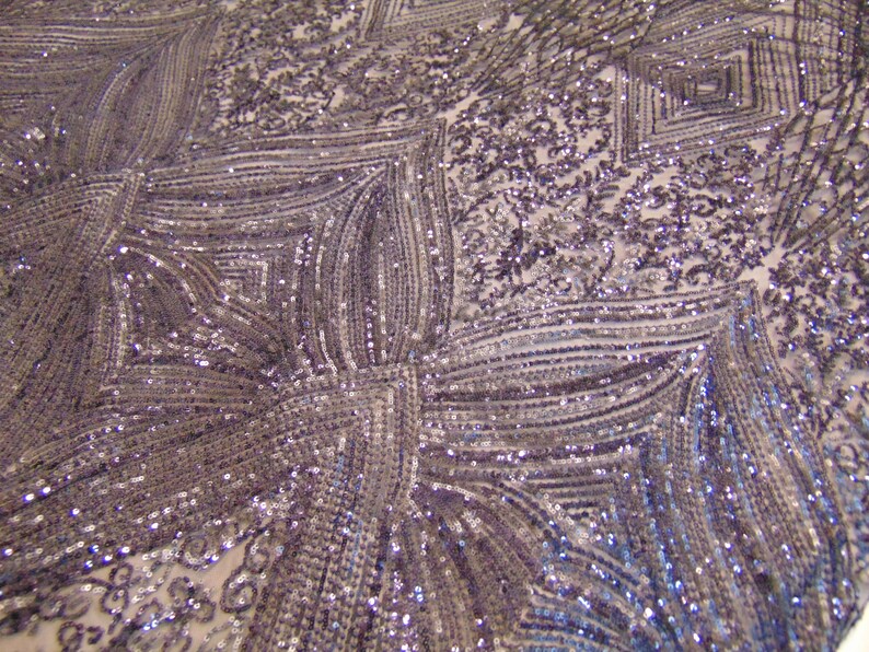 May include: A close-up of a silver sequined fabric with a geometric pattern. The sequins are arranged in a series of vertical lines and squares, creating a shimmering effect.