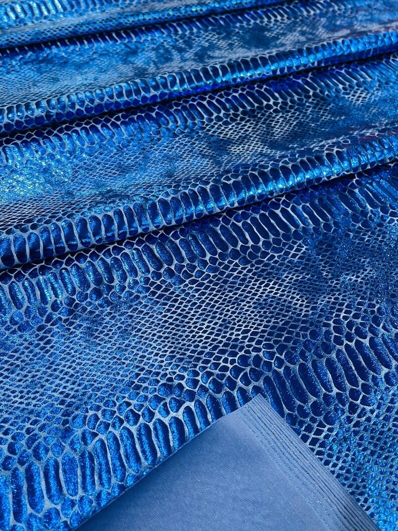 K&ouml;nnte beinhalten: Blauer, schimmernder Stoff mit Schlangenhautmuster. Der Stoff ist in mehreren Lagen gefaltet, wodurch die Textur und der Glanz des Materials sichtbar werden.