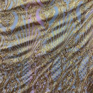 May include: White fabric with a gold glitter pattern. The pattern is a repeating design of ornate swirls and leaves.