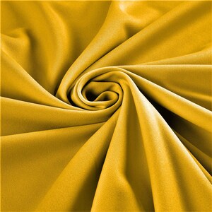 May include: A close-up of a smooth, yellow fabric with a soft, drapey texture. The fabric is folded and twisted, creating a swirling pattern.