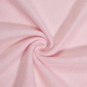 May include: Close-up of a swirl of soft, light pink fabric. The material appears to be a plush, possibly fleece or flannel, with a smooth texture and subtle folds. The fabric is evenly lit, highlighting its delicate color and texture.