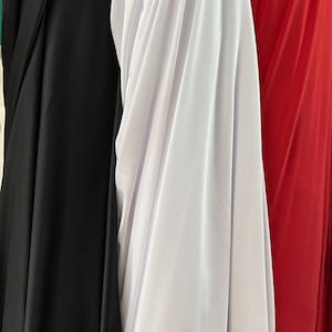 May include: Close-up of draped fabric in black, white, and red. The fabric has a smooth texture and hangs in soft folds. The colors are vibrant and the fabric appears to be lightweight, suitable for clothing or decorative projects.