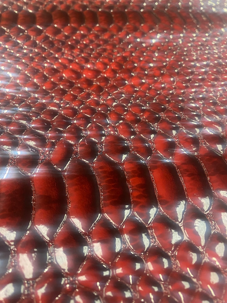 May include: Close-up of a glossy, red snakeskin pattern. The texture features a repeating scale design with a slight sheen, creating a luxurious and eye-catching appearance. The scales are slightly raised, adding depth to the surface.