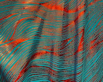 May include: Close-up of a teal fabric with a wavy pattern of copper-colored lines. The lines create a textured, flowing design across the surface. The fabric appears to be draped, with soft folds and shadows.