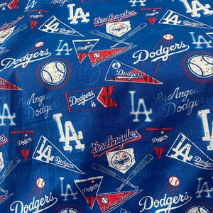 May include: Blue fabric featuring a repeating pattern of Los Angeles Dodgers baseball team logos, including the team name, the LA logo, baseballs, and crossed bats. The design incorporates red and white accents.