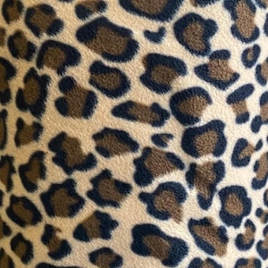 May include: A close-up of a brown and black leopard print fabric. The fabric has a soft, fuzzy texture.