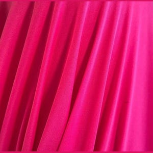 May include: Close-up of a vibrant fuchsia fabric with soft folds and a flowing texture. The material appears to be lightweight, possibly a chiffon or similar textile, with a slight sheen.