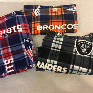 May include: Three fleece blankets with NFL team logos. The blankets are folded and feature the logos of the New England Patriots, Denver Broncos, and Las Vegas Raiders.