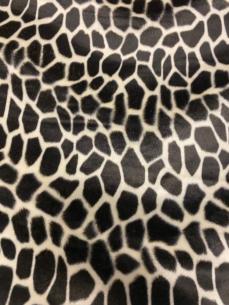 Puede incluir: Primer plano de una tela con un estampado de jirafa. El patr&oacute;n presenta formas negras irregulares sobre un fondo blanco, creando un dise&ntilde;o de alto contraste. La tela tiene un aspecto suave y texturizado.