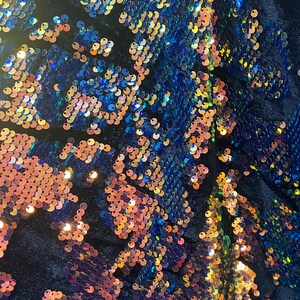 May include: A close-up of a fabric with iridescent sequins in shades of blue, gold, and pink. The sequins are arranged in a swirling pattern.