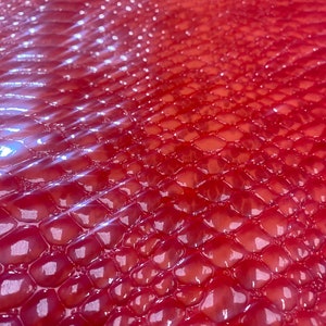 May include: Close-up of a red, textured surface with a repeating pattern of rounded, scale-like shapes. The surface has a glossy sheen, reflecting light and creating highlights. The overall effect is a vibrant, eye-catching texture.
