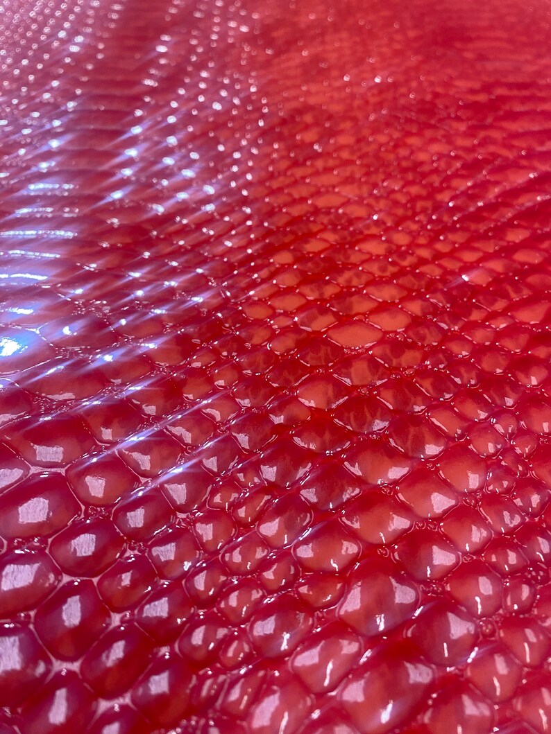May include: Close-up of a red, textured surface with a repeating pattern of rounded, scale-like shapes. The surface has a glossy sheen, reflecting light and creating highlights. The overall effect is a vibrant, eye-catching texture.