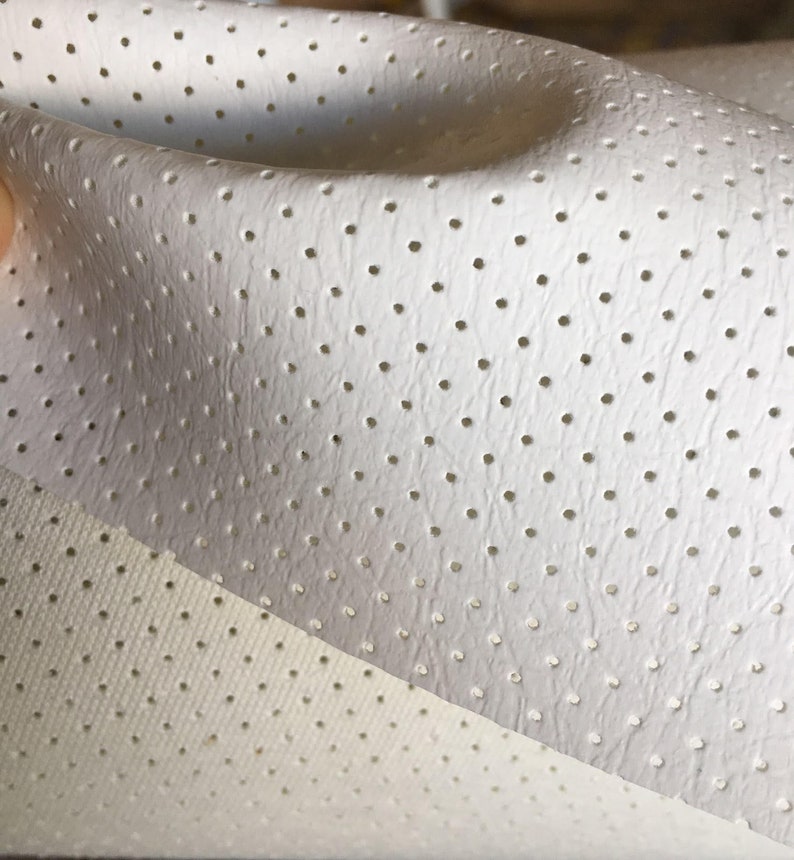 K&ouml;nnte beinhalten: Ein St&uuml;ck wei&szlig;es Material mit einer strukturierten Oberfl&auml;che, das ein gleichm&auml;&szlig;iges Muster aus kleinen, regelm&auml;&szlig;ig angeordneten kreisf&ouml;rmigen Perforationen aufweist. Das Material ist gefaltet und zeigt eine feinere netzartige Struktur.
