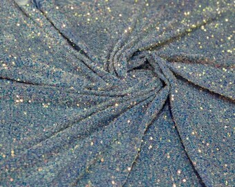 Può includere: Primo piano di un tessuto blu con superficie strutturata, densamente ricoperto di piccole paillettes iridescenti. Il tessuto è drappeggiato, creando pieghe e ombre che evidenziano l'effetto scintillante delle paillettes. Ideale per abbigliamento o progetti artigianali.