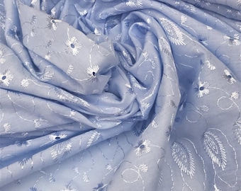 May include: A light blue fabric with intricate white floral embroidery and leaf patterns. The fabric is draped, showing the texture and design details. The embroidery adds a delicate touch to the soft material, creating a visually appealing textile.