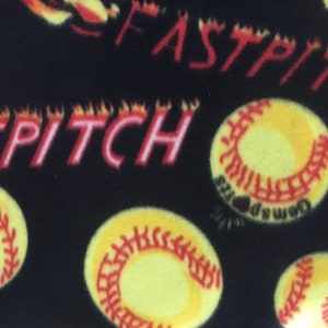 May include: Black fabric with yellow softballs and the words "FAST PITCH" in red, with flames. The softballs have red stitching and the word "Gemsports" printed on them. The overall theme is softball.