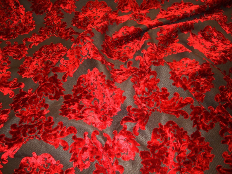 Pode incluir: Tecido de veludo vermelho com um padr&atilde;o de damasco sobre um fundo preto. O tecido &eacute; drapeado e mostra a textura do veludo.