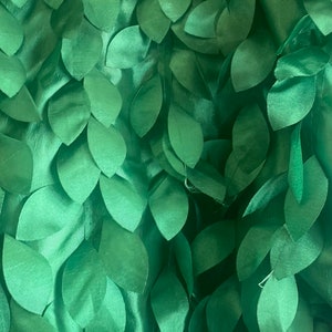 May include: Green fabric with a 3D leaf design. The leaves are made of a soft, silky material and are arranged in a random pattern.