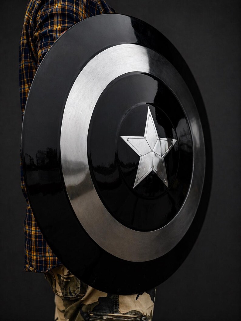 Puede incluir: Un escudo negro y plateado con un dise&ntilde;o de estrella central. El escudo tiene forma circular con un anillo plateado alrededor del borde. La estrella es plateada y tiene cinco puntas. Es un accesorio o art&iacute;culo de colecci&oacute;n.