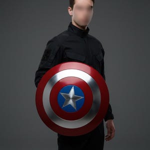 May include: A round shield with a red outer ring, a silver inner ring, and a blue center featuring a white star. The shield is held by a person wearing a black jacket and pants.