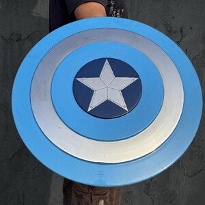 May include: A blue, silver, and white shield with a central star design. The shield has a circular shape with concentric rings of colour. The centre is dark blue with a white star.