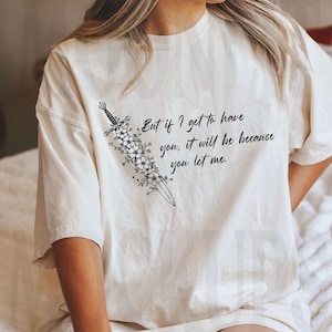 May include: Cream-colored t-shirt featuring a black floral sword design and the quote, "But if I get to have you, it will be because you let me." The shirt has a relaxed fit.