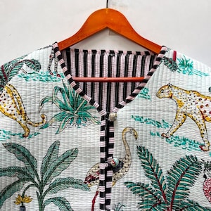 Pode incluir: Um casaco acolchoado com base branca e uma estampa colorida de guepardos, zebras, flamingos e palmeiras tropicais. A peça possui decote em V, mangas compridas e um fecho frontal de botões com botões estampados e acabamento em preto e branco.