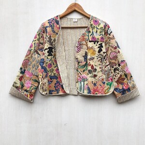Può includere: Una giacca corta caratterizzata da un design patchwork con vari motivi floreali e astratti nei toni del rosa, giallo, blu e verde. Il capo presenta maniche lunghe, uno scollo rotondo e una fodera interna visibile con sottili righe verticali.