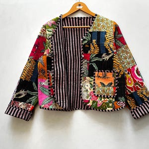 Könnte beinhalten: Eine langärmelige Steppjacke mit Patchwork-Design, das verschiedene Blumen- und Tigermuster in leuchtenden Farben zeigt. Die Jacke hat ein schwarz-weiß gestreiftes Innenfutter, einen Rundhalsausschnitt und eine einzelne Vordertasche.