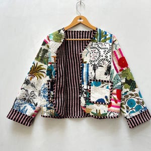 Könnte beinhalten: Eine gesteppte Jacke mit Patchwork-Design, das verschiedene botanische und abstrakte Muster in Blau-, Grün-, Rot- und Weißtönen aufweist. Die Jacke hat lange Ärmel, einen Rundhalsausschnitt, zwei Vordertaschen und ein schwarz-weiß gestreiftes Innenfutter.