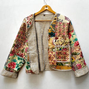 Könnte beinhalten: Eine gesteppte Jacke mit Patchwork-Design und verschiedenen Blumenmustern in Rot-, Gelb-, Grün- und Blautönen. Die Jacke hat lange Ärmel, eine offene Vorderseite und ein kontrastierendes Innenfutter mit dünnen, schwarzen vertikalen Streifen.