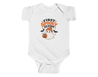 May include: A white short-sleeved baby bodysuit featuring a graphic of a ghost wearing an orange beanie and holding a jack-o'-lantern. The text reads FIRST SPOOKY SEASON in orange and black lettering, surrounded by small black bats and stars.