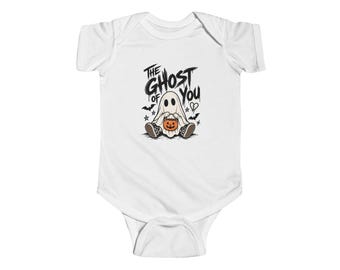 May include: A white short-sleeved baby bodysuit featuring a graphic of a ghost wearing trainers and holding an orange jack-o'-lantern bucket. The text reads THE GHOST OF YOU, accompanied by small illustrations of bats, stars, and a broken heart.
