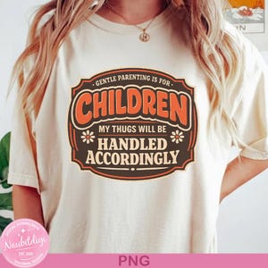 May include: Cream-colored t-shirt with a retro-style graphic. The graphic reads "GENTLE PARENTING IS FOR CHILDREN, MY THUGS WILL BE HANDLED ACCORDINGLY" in orange and brown lettering. The shirt has a relaxed fit and short sleeves.