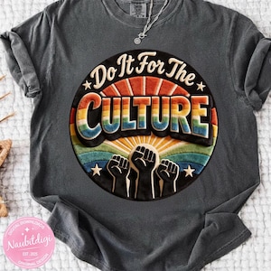 May include: Dark gray t-shirt with a colorful graphic that reads "Do It For The CULTURE." The design features a rainbow, stars, and raised fists. A silver necklace is visible. The shirt has a vintage, washed look.
