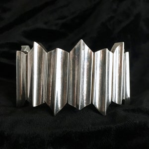 May include: A silver bracelet with a geometric design. The bracelet is made of multiple connected pieces that form a series of points.