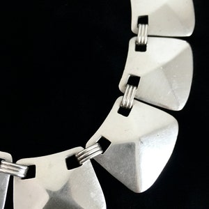 May include: A silver necklace with geometric, square-shaped links. The links are connected by a series of smaller, twisted silver rings.