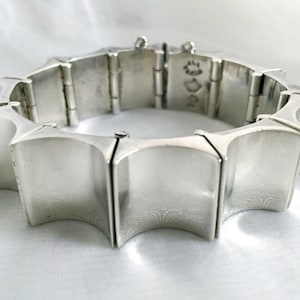 May include: A silver bracelet with a geometric design. The bracelet is made of interlocking pieces that form a starburst pattern. The bracelet is marked with the letters "D" and "R" on the clasp.