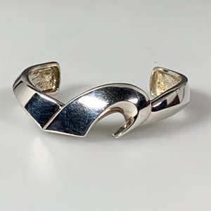 May include: A silver bracelet with a wave-like design. The bracelet is open and has a simple, modern style.