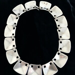 May include: A silver necklace with square links. The links are connected by a thin silver chain. The necklace has a clasp on the back.