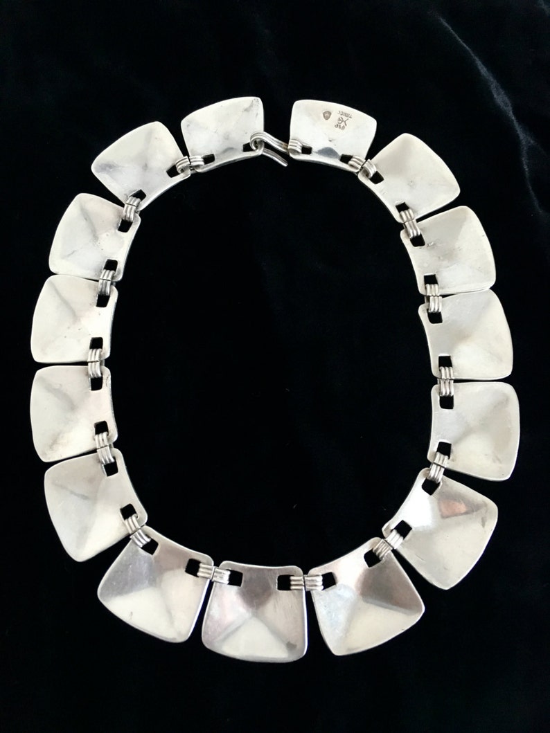 May include: A silver necklace with square links. The links are connected by a thin silver chain. The necklace has a clasp on the back.