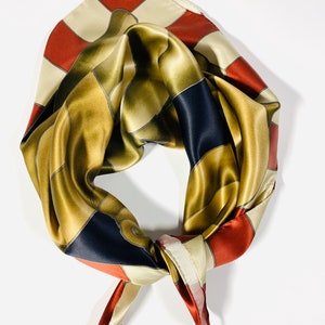 May include: A silk scarf in gold, red and cream colours with a geometric pattern. The scarf is tied in a knot.