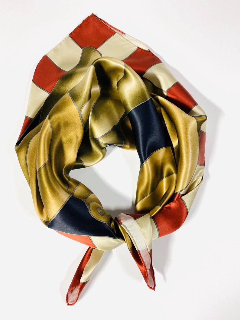 May include: A silk scarf in gold, red and cream colours with a geometric pattern. The scarf is tied in a knot.