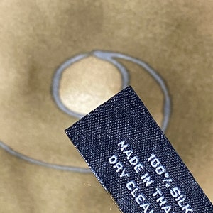 May include: A black fabric label with white text that reads "100% Silk Made in Thailand Dry Clean Only".