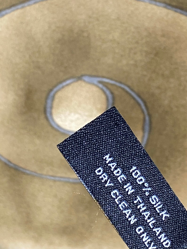 May include: A black fabric label with white text that reads "100% Silk Made in Thailand Dry Clean Only".