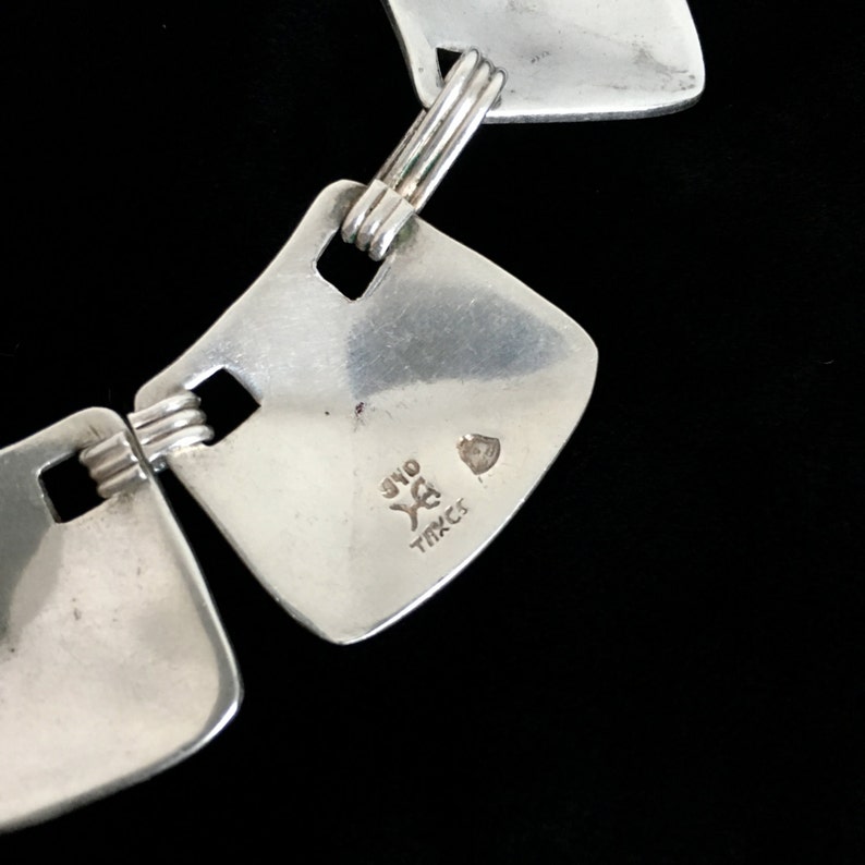 May include: Close-up of a silver bracelet with square links. The bracelet is stamped with "925" and "T.M.C.S."