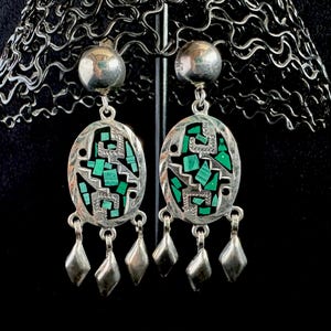 May include: A pair of silver dangle earrings with green malachite stone inlays. The earrings feature a geometric design and are accented with four silver teardrop-shaped charms.